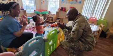 Command Sgt. Maj. Shelly Jenkins, Fort Drum garrison senior enlisted adviser, entertains a toddler during a routine inspection of a Family Child Care home. (Photo by Mike Strasser, Fort Drum Garrison Public Affairs)